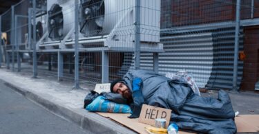 Dirty homeless with help sign lies on city street