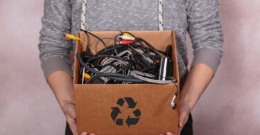 Female hands carrying cardboard box filled with old digital devices