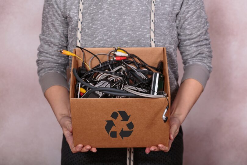Female hands carrying cardboard box filled with old digital devices