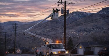 Utility crew in a bucket truck repairing power lines near Colorado Front Range homes at dusk