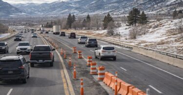 Vehicles travel on a Northern Colorado interstate past orange cones with Front Range foothills in the distance