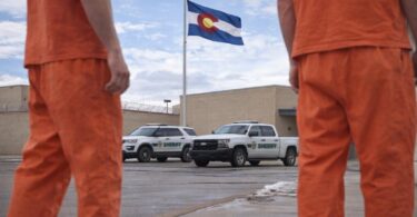County jail exterior in Northern Colorado with Colorado flag and sheriff vehicles parked outside on a clear day