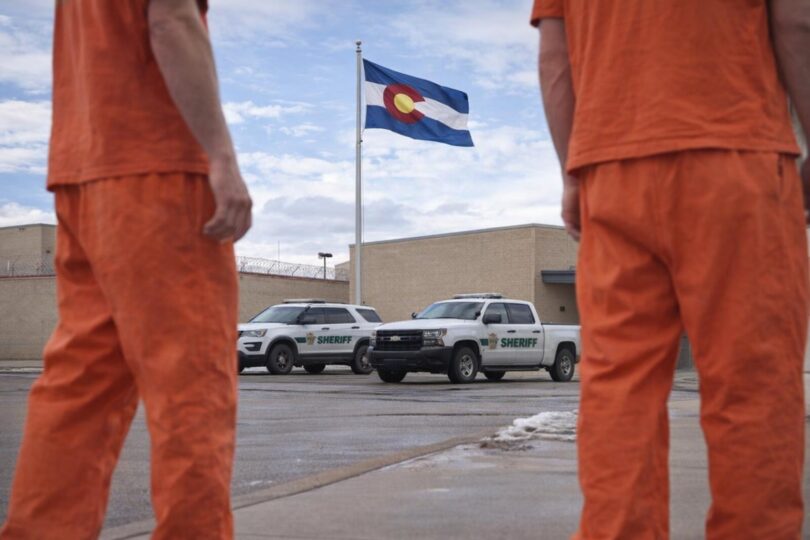County jail exterior in Northern Colorado with Colorado flag and sheriff vehicles parked outside on a clear day
