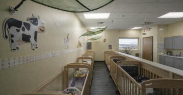 A quiet childcare infant room with empty cribs and bright yellow walls in Colorado