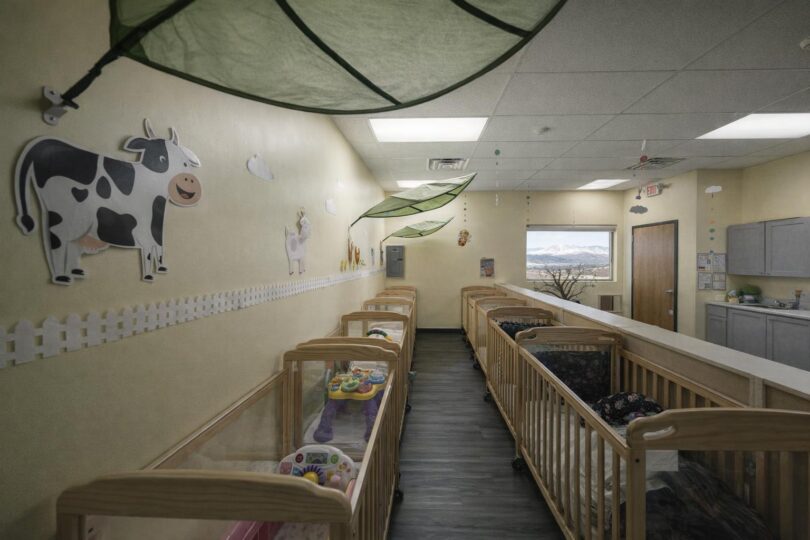 A quiet childcare infant room with empty cribs and bright yellow walls in Colorado