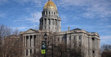 State office desk with audit papers and a Colorado government building backdrop