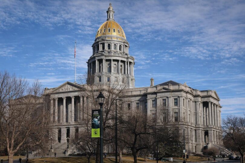 State office desk with audit papers and a Colorado government building backdrop