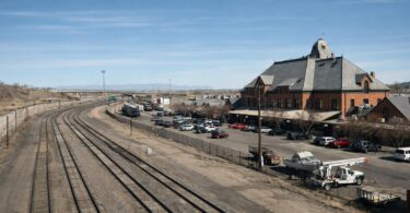 Passenger train tracks across Colorado Front Range plains with mountains in the distance.