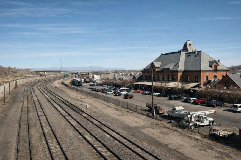 Passenger train tracks across Colorado Front Range plains with mountains in the distance.