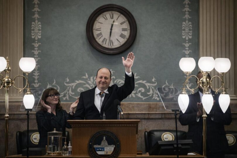 Lawmakers in a Colorado budget meeting with papers and the State Capitol nearby