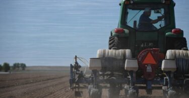 Colorado farmer standing in a dry field with irrigation equipment nearby