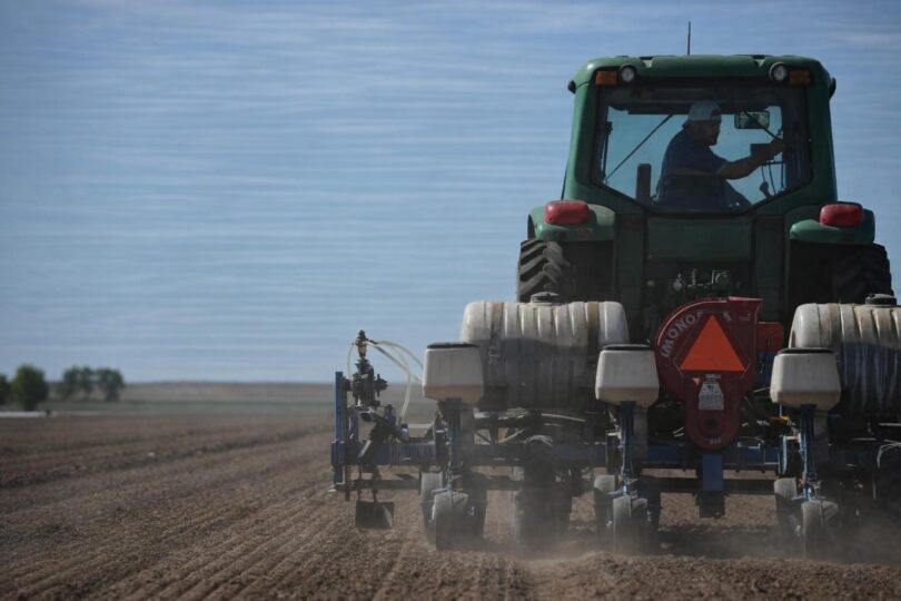 Colorado farmer standing in a dry field with irrigation equipment nearby
