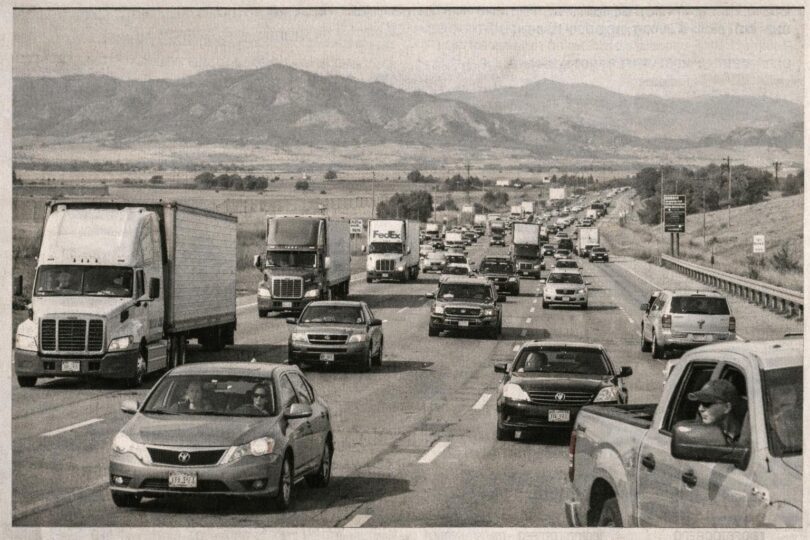 Cars and trucks on a Colorado highway corridor with open plains and Front Range views.