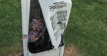 Damaged telecommunications pedestal near a Colorado roadway after copper wire theft